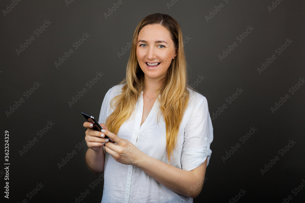 Happy mature woman holding smartphone using mobile on grey studio background