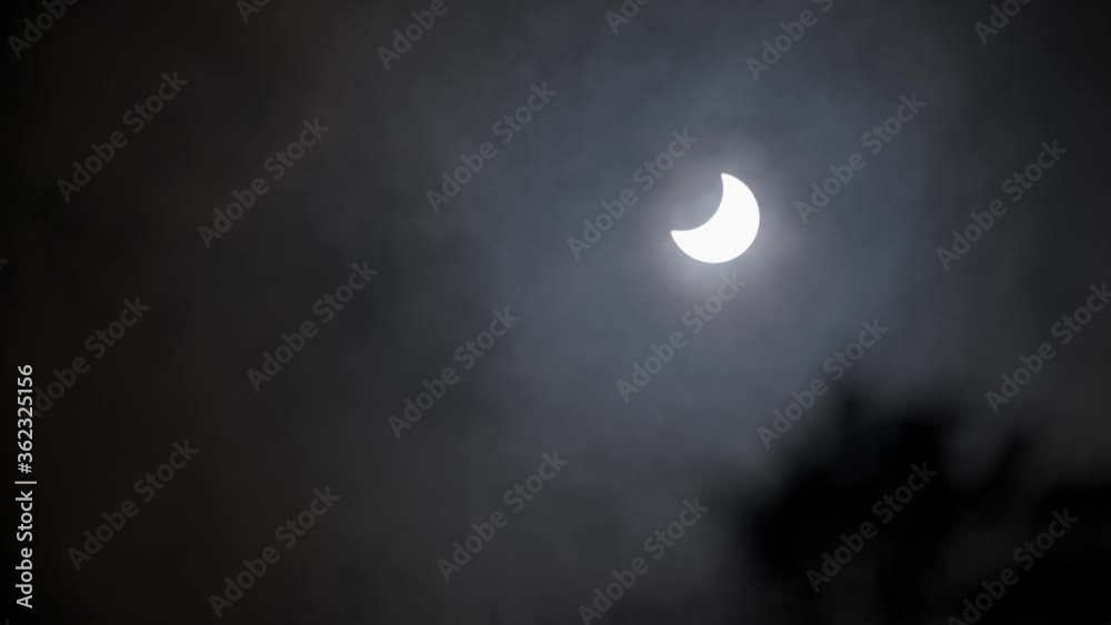 Clouds passing in front of a partial solar eclipse trees blowing in the foreground Clouds passing in front of a partial solar eclipse trees blowing in the foreground