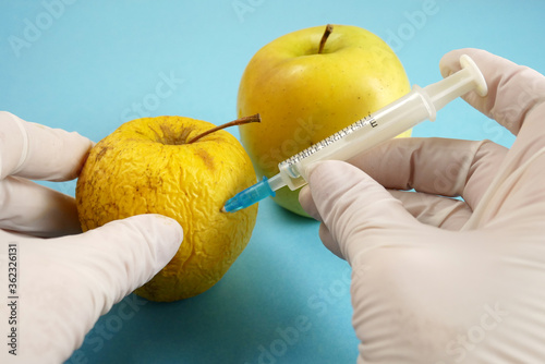 apple in genetic engineering laboratory with syringe and test tubes on blue background, gmo food concept