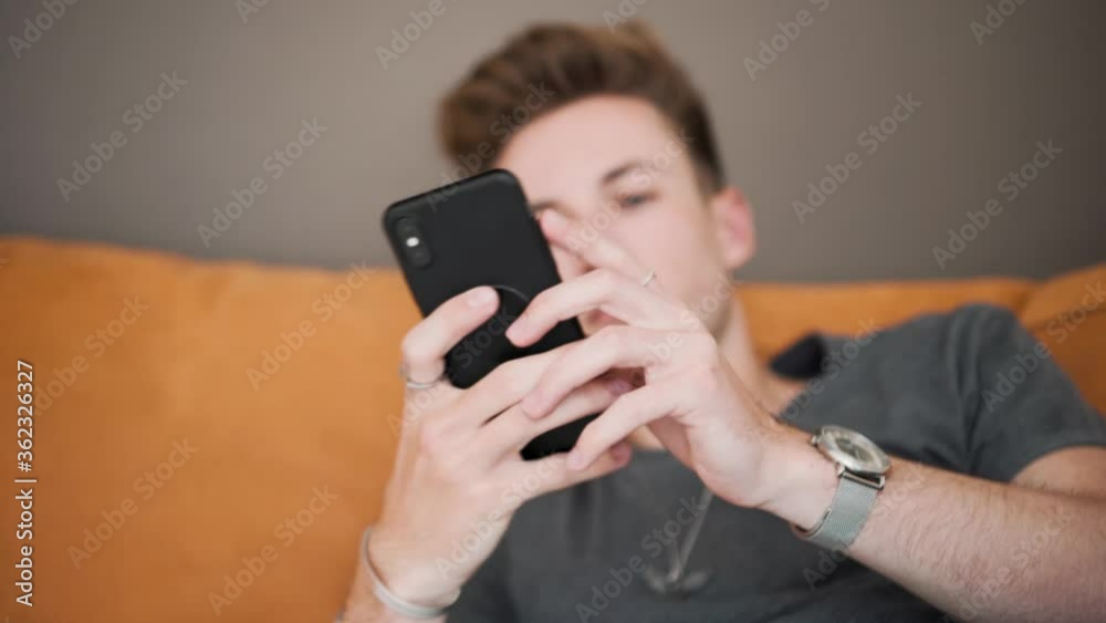 Close up shot of a handsome man sitting on a couch and using his smartphone Close up shot of a handsome man sitting on a couch and using his smartphone