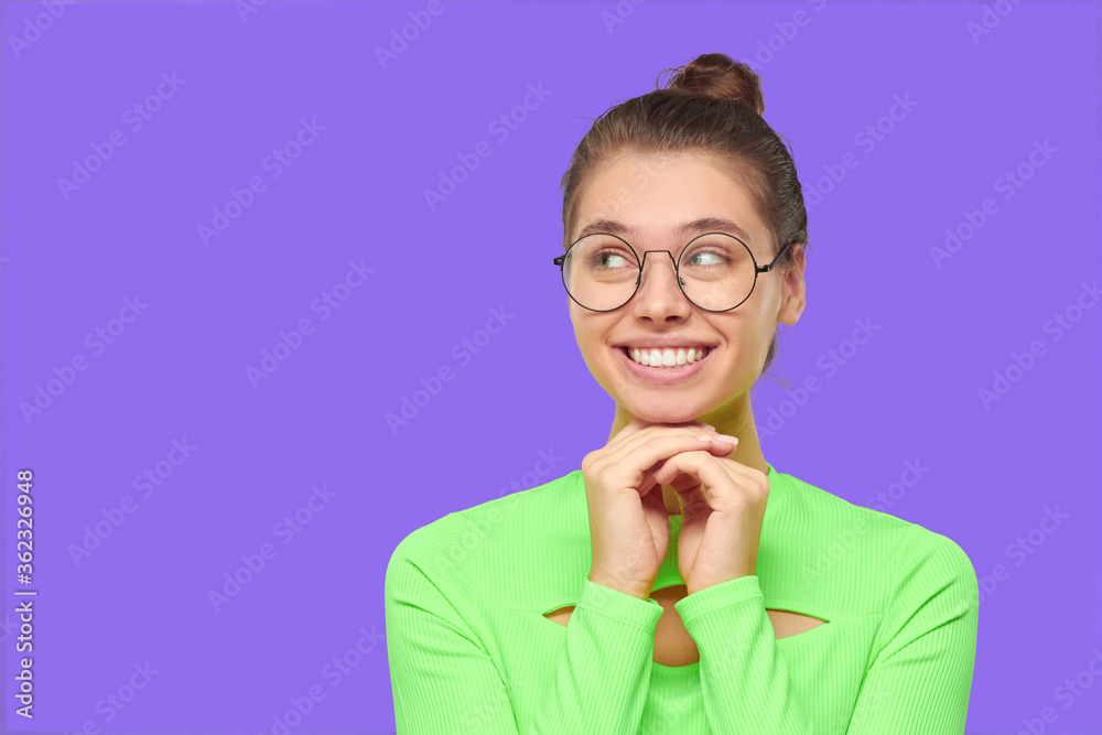 Young girl holding hands together as if hoping and making wish, looking away dreaming, isolated on purple background with copy space Young girl holding hands together as if hoping and making wish, looking away dreaming, isolated on purple background with copy space