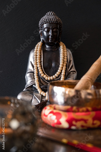 Jet black Buddha with bead collar next to a tibetan singing bowl and incense sticks. photo