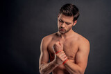 Handsome young bearded man isolated. Cropped image of topless muscular man is standing on gray background. Man holding his wrist. Experiencing wrist pain.