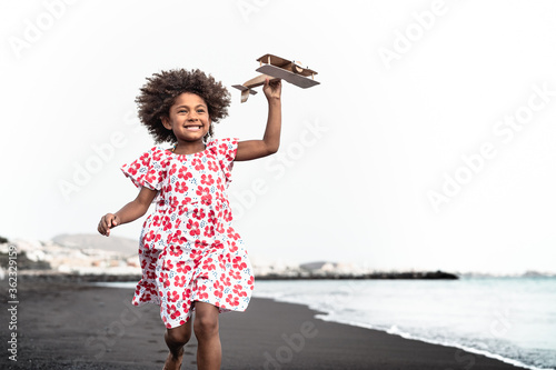 Foto Afro child playing with wood toy airplane on the beach - Little kid having fun d