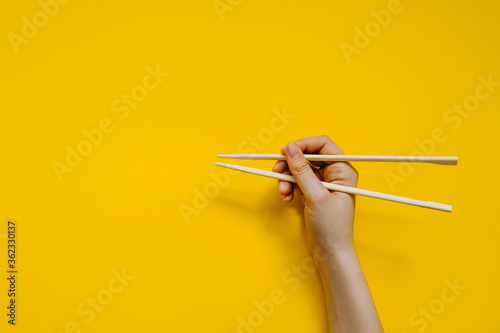 Human hand using chopsticks, on clean yellow background. Learning how to use chopsticks.