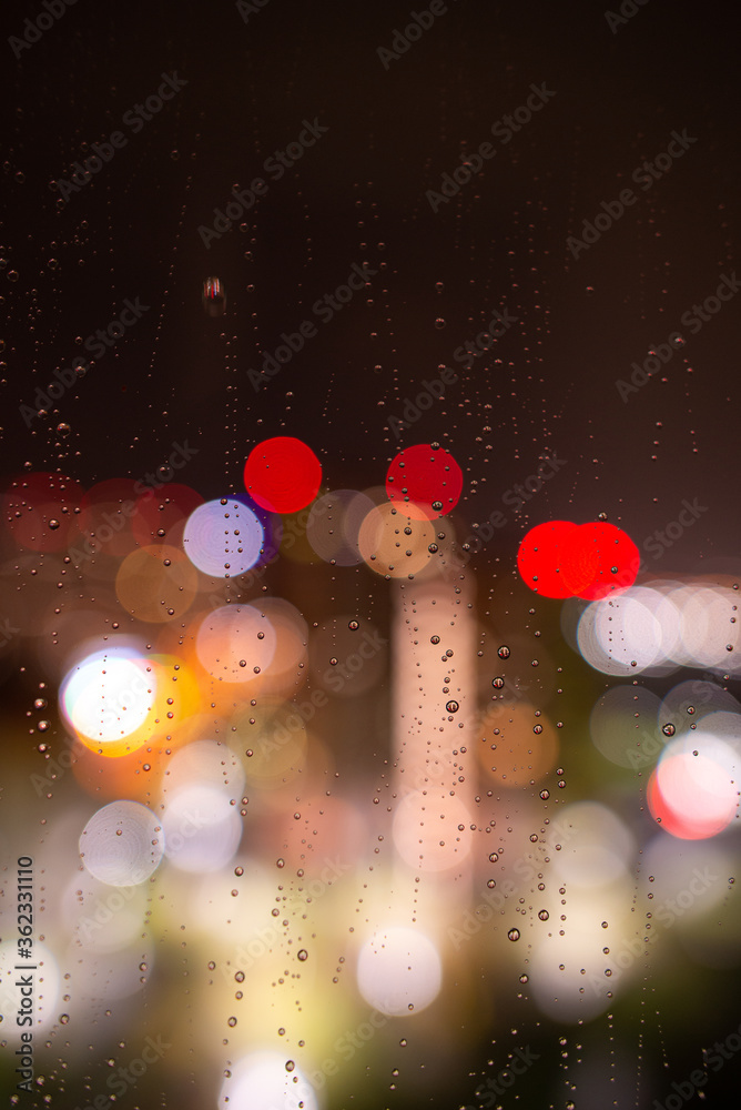 Raindrops on the window glass at night against the background of bokeh from the lights and Windows of the houses opposite