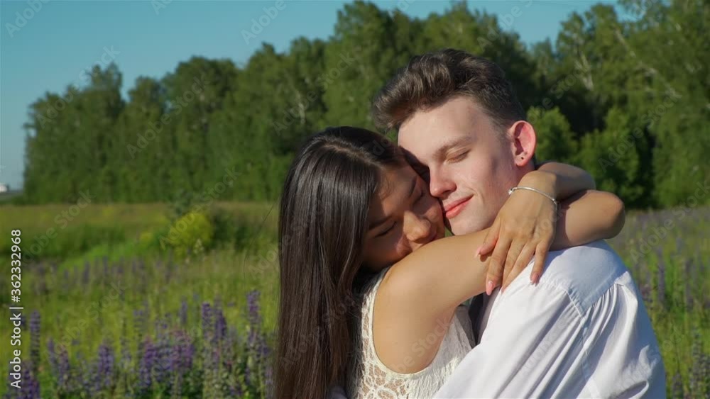 Happy Couple of Teenagers Hugging in a Summer Field. Young Asian Girl with Caucasian Boyfriend Enjoying Time Together. Slow Motion. Happy Couple of Teenagers Hugging in a Summer Field. Young Asian Girl with Caucasian Boyfriend Enjoying Time Together. Slow Motion.