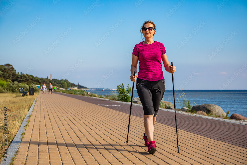 Nordic walking - middle-aged woman training by the sea shore Stock Photo |  Adobe Stock