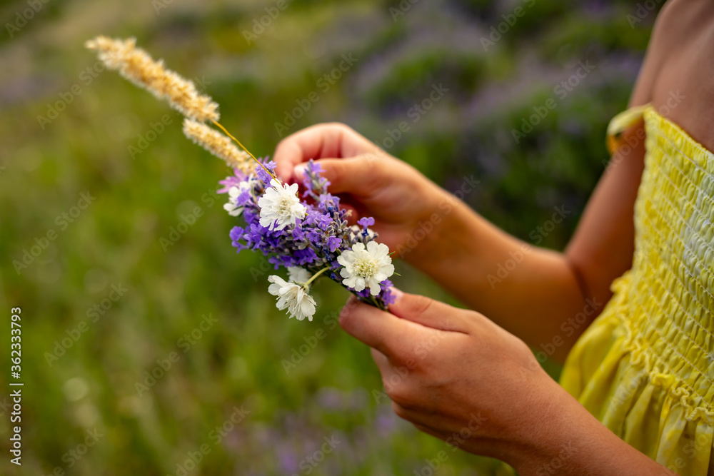 A small bouquet of wildflowers in the hands of a girl in a yellow dress in the evening light. A small bouquet of wildflowers in the hands of a girl in a yellow dress in the evening light.