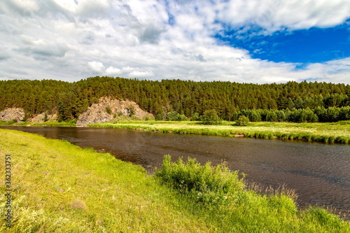 River in summer on the background of rocks, pines, white clouds