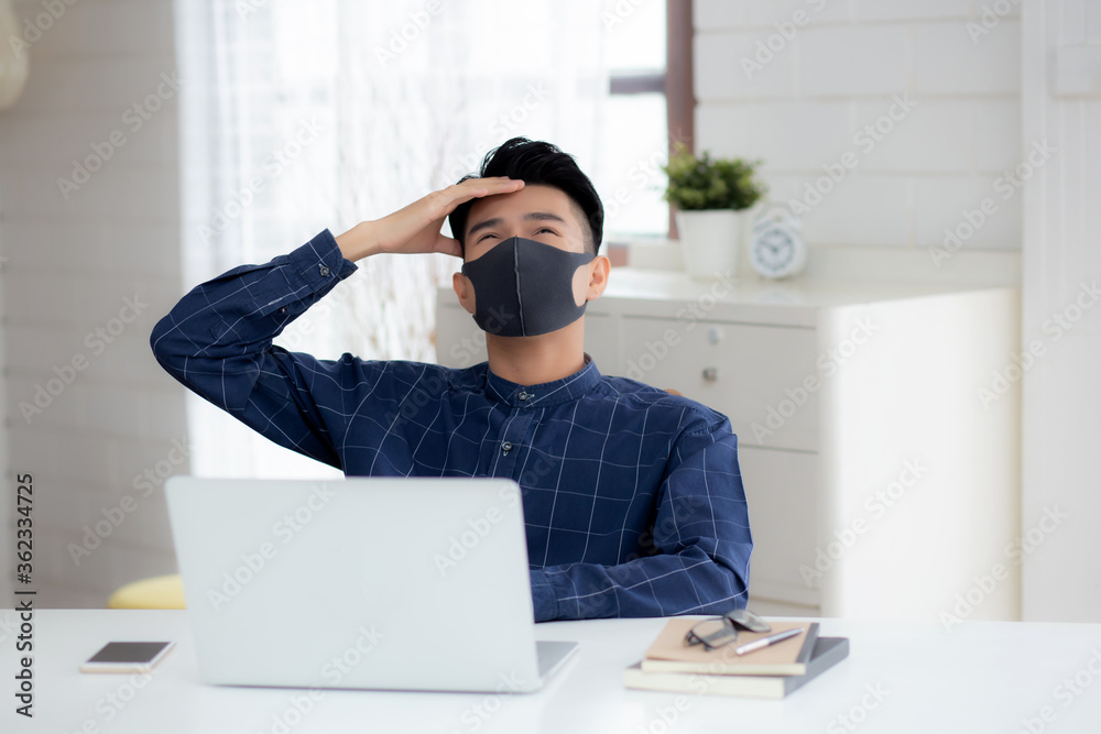 Young business man in face mask working from home with laptop computer and bored on desk for protection for outbreak of covid-19, male quarantine stay home using notebook with unhappy, new normal.