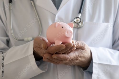 Close up of male doctor in white medical uniform hold piggybank ask about volunteer money donation for hospital or clinic, man GP collect charity contribution for patient care, healthcare concept