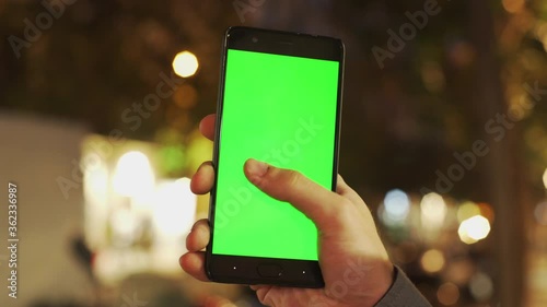 Wallpaper Mural Young man using vertical smartphone with chroma key mock-up, doing swiping and tapping gestures on greenscreen technologies. Wonderful urban cityscape blurred bokeh background Torontodigital.ca