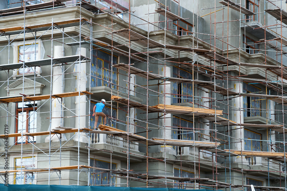 construction worker is on scaffold, modern building under construction, plastered walls and scaffolding