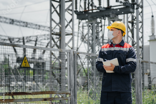 An electrical substation engineer inspects modern high-voltage equipment in a mask at the time of pondemia. Energy. Industry