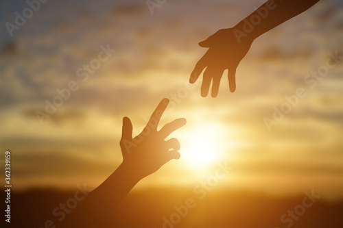 Silhouette of giving a helping hand, hope and support each other over sunset background.