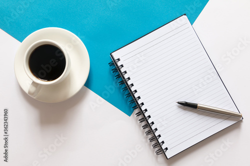 Flay lay of coffee  blank notebook and pen on split color blue and white background