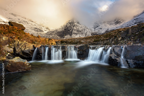Stunning cascade waterfall at the Fairy Pools on the Isle of Skye in the Scottish Highlands. Taken in the evening golden hour  beautiful light from the sun can be seen in the Winter landscape.