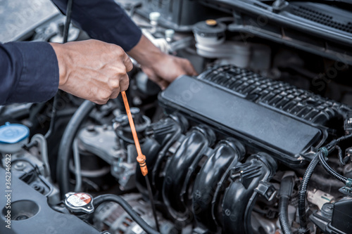 Auto mechanic checking vehicle’s engine oil level to changing car engine oil concepts of maintenance repair service and car insurance.