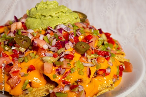 Closeup shot of nacho toppings with cheese, peppers, onions, tomatoes, and guacamole photo