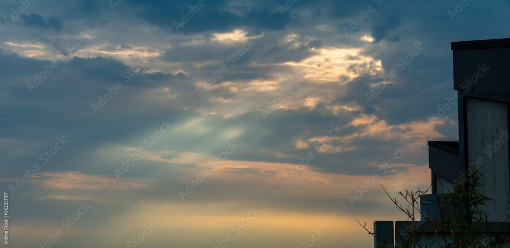 Rays of light piercing through the clouds during sunset with parts of rooftops