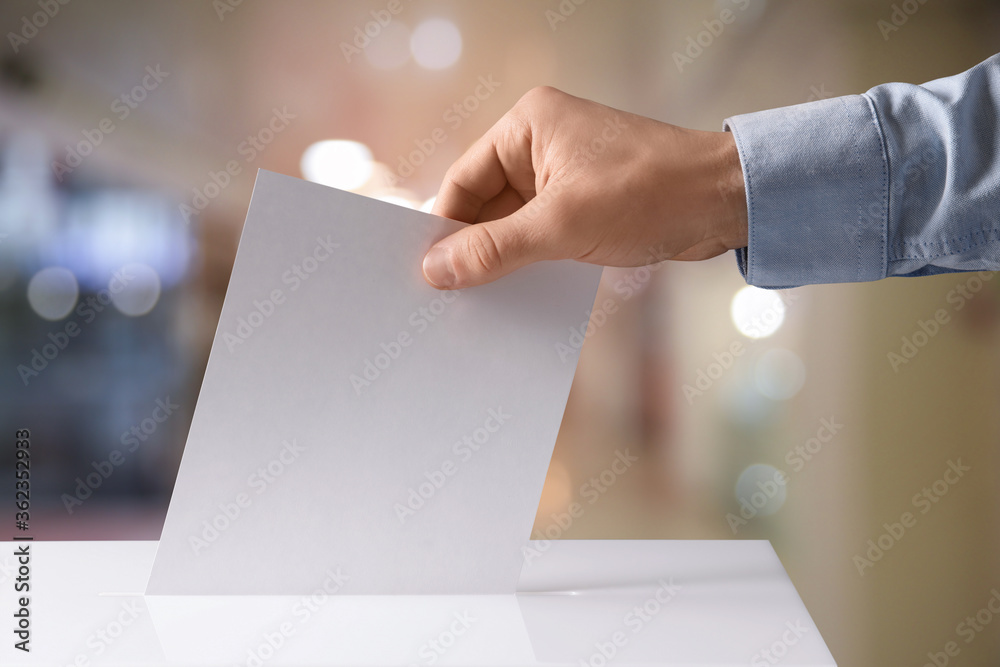 Man putting his vote into ballot box indoors, closeup Man putting his vote into ballot box indoors, closeup