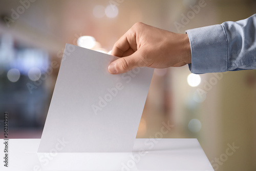 Man putting his vote into ballot box indoors, closeup