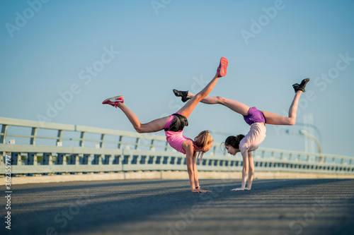 Two teenage girls perform an acrobatic element outdoors against a blue sky