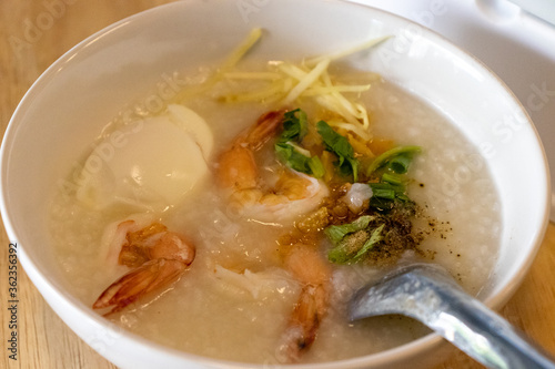 boiled rice soup with shrimp in white bowl on wooden table