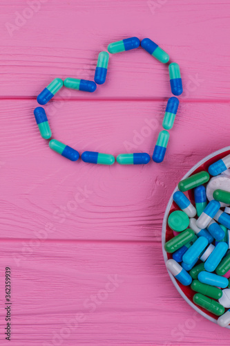 Topview heart made of colored pills. Pink wooden background.