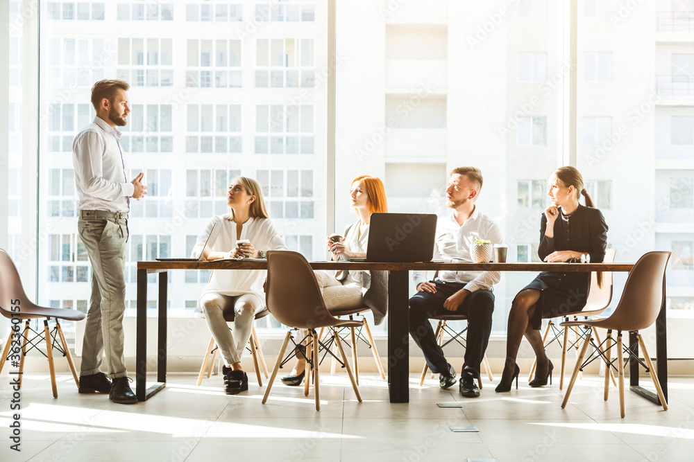 A team of young businessmen working and communicating together in an office. Corporate businessteam and manager in a meeting. desktop against the background of the pan window, free space for text A team of young businessmen working and communicating together in an office. Corporate businessteam and manager in a meeting. desktop against the background of the pan window, free space for text