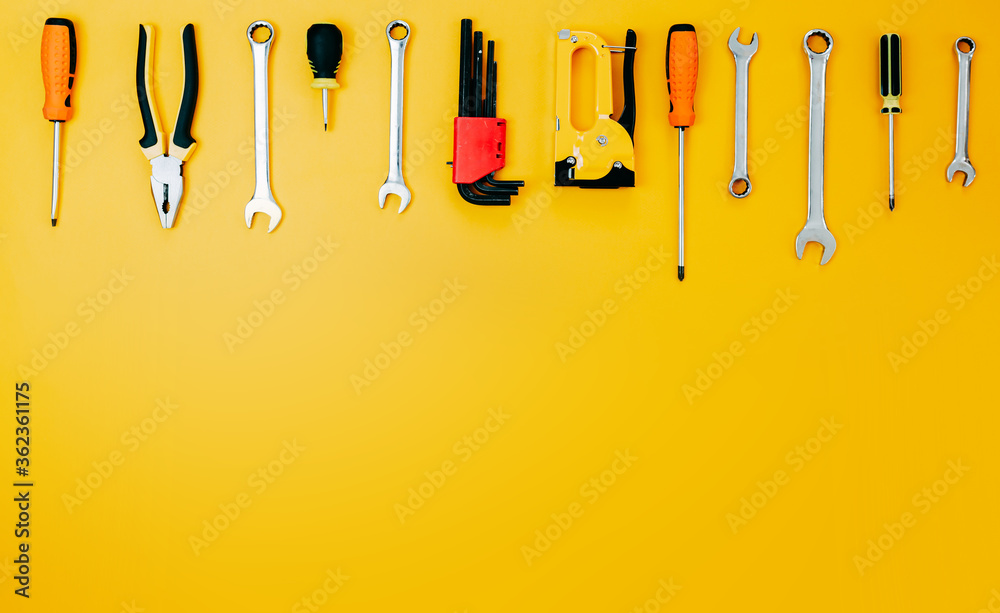 Tools top view on yellow background. Plier, open wrenches, screwdrivers and staple gun flat lay with copy space.