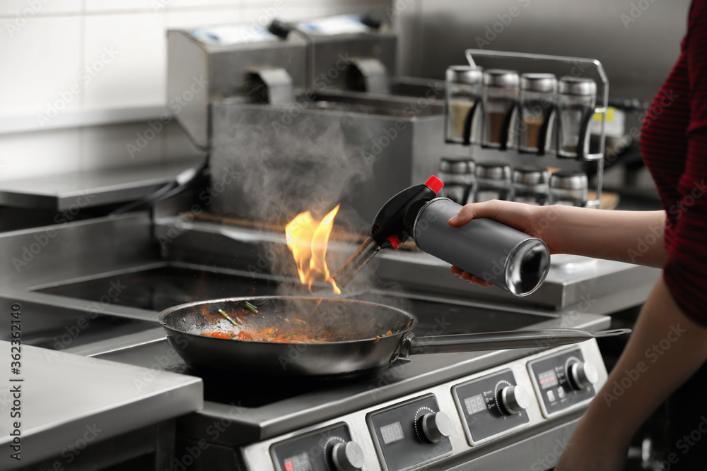 Female chef with manual gas burner cooking tasty food on stove in restaurant kitchen, closeup Female chef with manual gas burner cooking tasty food on stove in restaurant kitchen, closeup