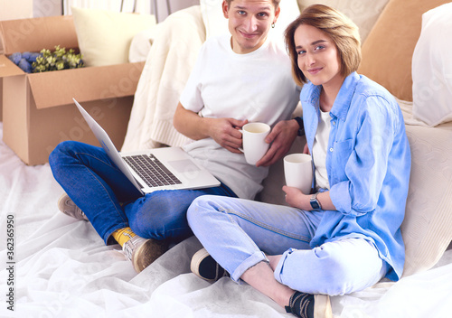 Couple buying online with a laptop and moving house sitting on the floor