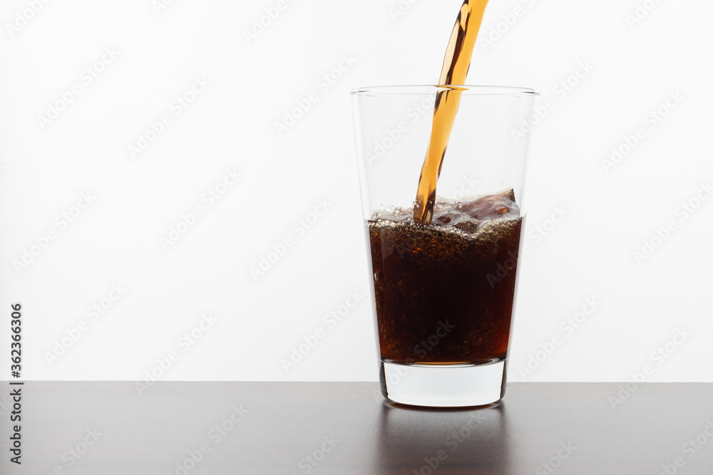 Cola drink pouring into a transparent glass on a wooden table on a white background Cola drink pouring into a transparent glass on a wooden table on a white background