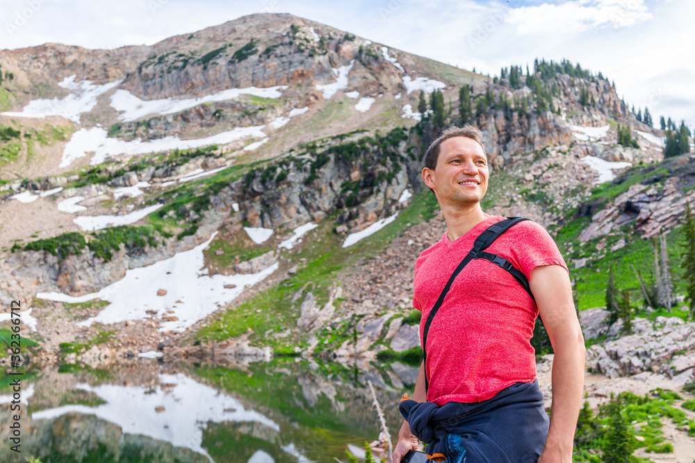 Naklejka premium Albion Basin, Utah summer with happy man standing looking at view by reflection of water on Cecret Lake in Wasatch mountains with rocks, snow and green color