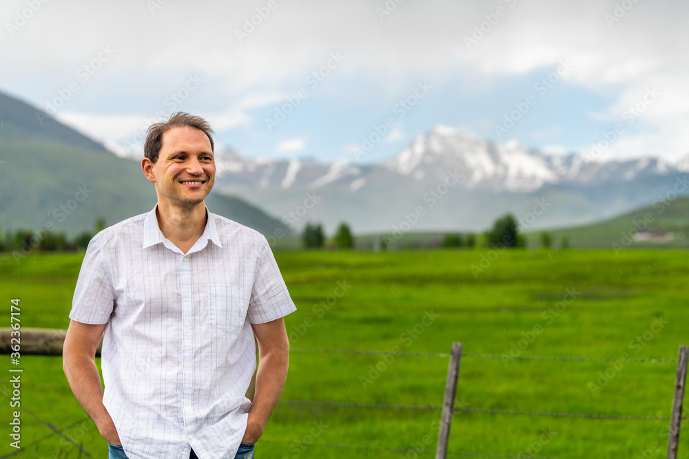 Obraz premium Crested Butte, Colorado near Gunnison countryside with happy man standing by rural fence in summer on cloudy day with green grass and mountain view