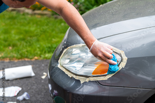 Obraz na plátně Man person worker cleaning car headlights taped to protect paint rubbing with bl