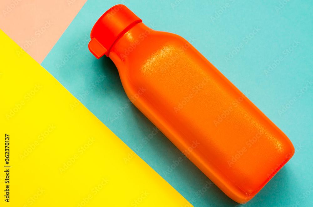 Orange plastic bottle for water close-up. Bottle on a three-color background. Orange plastic bottle for water close-up. Bottle on a three-color background.
