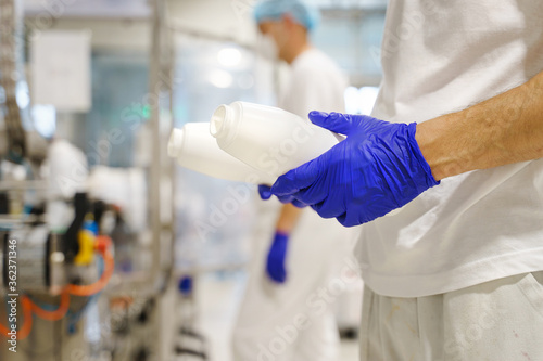 Close up on hands of unknown caucasian man holding bottle container while working at factory - Food production blue rubber protective gloves on hands as hygiene procedure at work - safety concept