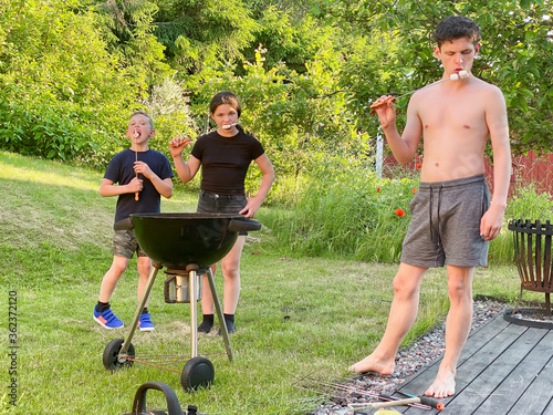 Teenager and children relaxing.  Hot summer garden marshmallows barbecue grill in meadow backyard.