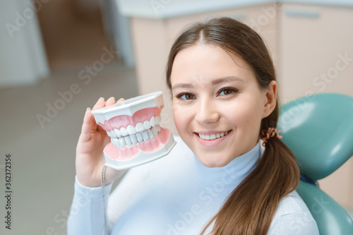 Beautiful young woman in dental chair. Smiling and satisfied patient at dentist's office after treatment. Healthy teeth, dental care concept.