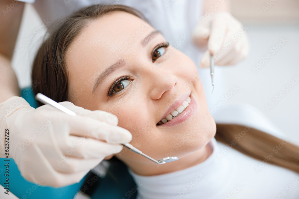 Patient in dental chair. Dentist's hands in gloves work with a dental tools. Beautiful young woman having dental treatment at dentist's office. Patient in dental chair. Dentist's hands in gloves work with a dental tools. Beautiful young woman having dental treatment at dentist's office.