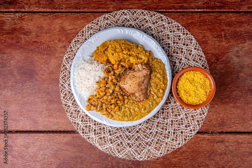 Fototapeta Naklejka Na Ścianę i Meble -  Delicious Caruru. Traditional Afro-Brazilian dish made with okra and dried shrimp, accompanied by vatapa, beans, rice, chicken and farofa. On a wooden table.
