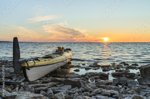 Fototapeta Naklejka Na Ścianę i Meble -  Yellow plastic tandem sea kayak parked on rocky shore. Sunset glow on the Baltic Sea water. North coast of tiny Kesselaid (Kessulaid) islet in Suur Strait. Typical Estonian coastline. Dawning sky.