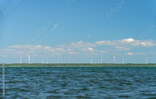 Virtsu wind farm. Turbine park next to harbor photographed from the water of Suur Strait. Warm midsummer day, blue sky, calm sea. Landmarks visible from far. Estonian coastal area. © Ingrid