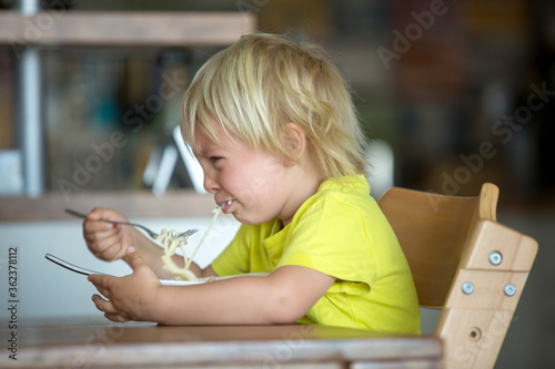 Εκτύπωση καμβά Cute blond boy, child eating spaghetti, crying with tantrum
