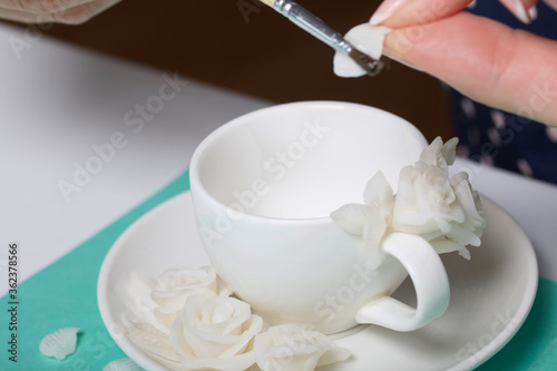 Roses with petals made of white polymer clay. A woman sticks them on a mug. Crafts from polymer clay.