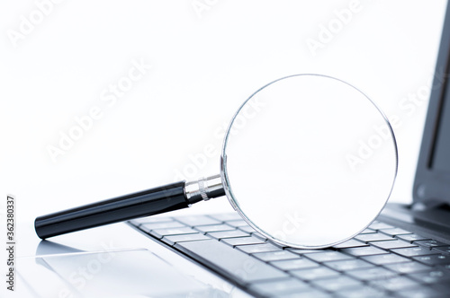 magnifier lies on a laptop keyboard. Technology, business concept.