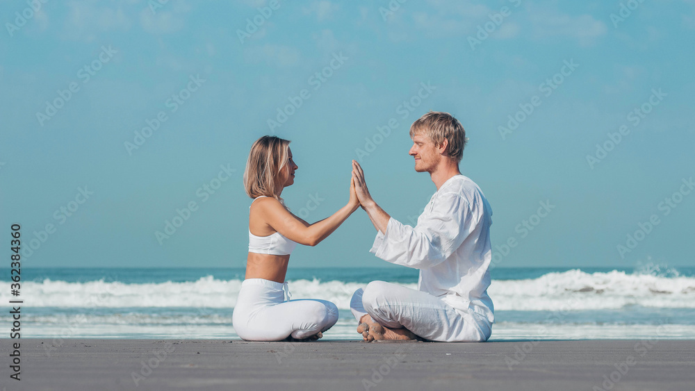 Fototapeta premium guy and girl in white clothes are sitting on the ocean and holding hands namaste